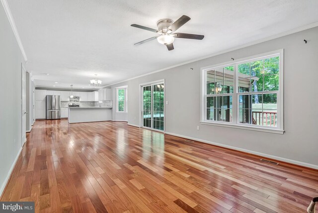 unfurnished living room featuring crown molding, a chandelier, light wood-style floors, ceiling fan, and baseboards
