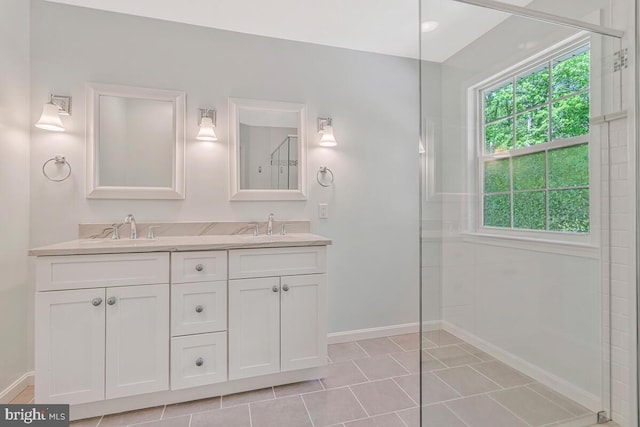 full bath featuring baseboards, double vanity, a tile shower, and tile patterned flooring