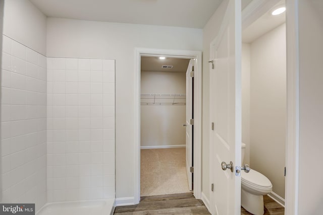 full bathroom with visible vents, walk in shower, toilet, a walk in closet, and wood finished floors