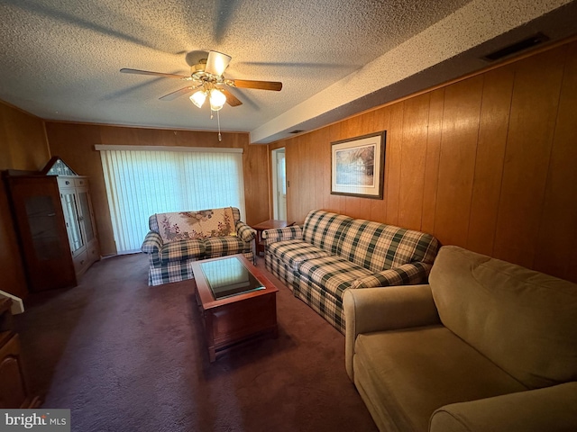 living room with visible vents, ceiling fan, a textured ceiling, wooden walls, and carpet floors