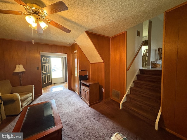 living area featuring ceiling fan, a textured ceiling, visible vents, carpet floors, and stairs