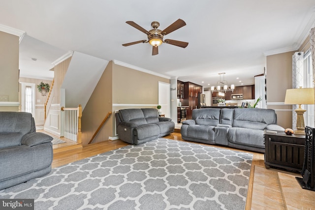 living room featuring a healthy amount of sunlight, ornamental molding, light wood finished floors, and ceiling fan with notable chandelier