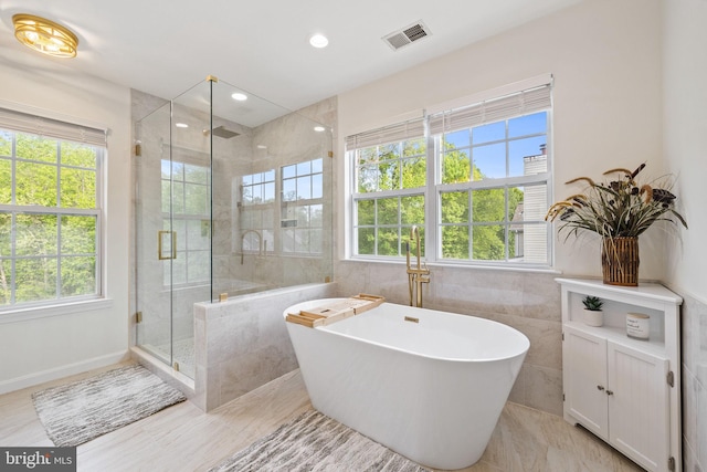full bath with tile walls, visible vents, and plenty of natural light