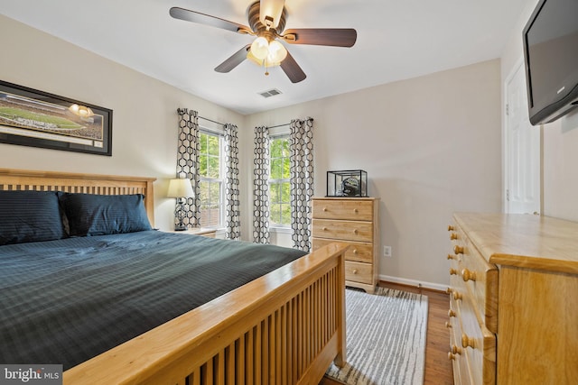 bedroom with baseboards, a ceiling fan, visible vents, and wood finished floors