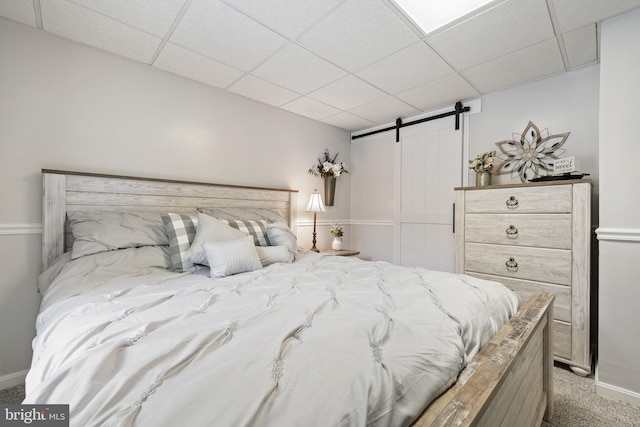 carpeted bedroom with a paneled ceiling, baseboards, and a barn door