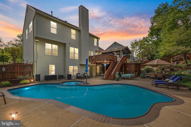 pool at dusk featuring a fenced in pool, an in ground hot tub, a patio, stairway, and a wooden deck
