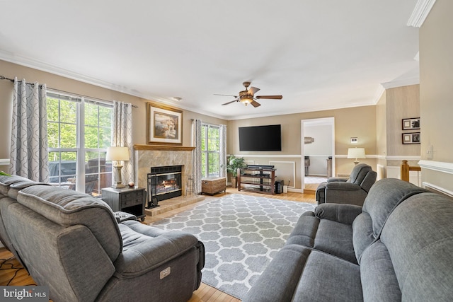 living room with light wood finished floors, ornamental molding, ceiling fan, and a tile fireplace