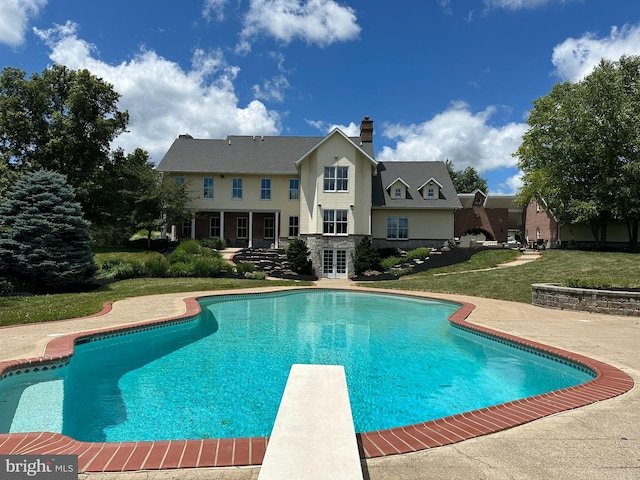 outdoor pool with a lawn, a diving board, and french doors