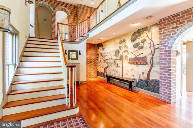 staircase featuring arched walkways, wood finished floors, baseboards, visible vents, and a high ceiling
