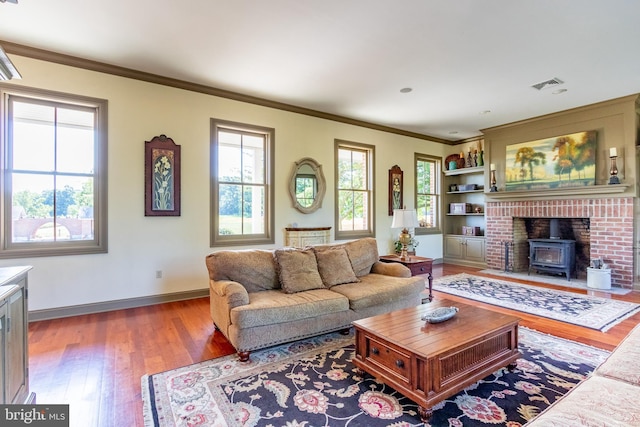 living area featuring wood finished floors, ornamental molding, baseboards, visible vents, and a wood stove
