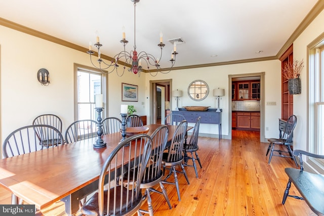 dining room with visible vents, ornamental molding, a notable chandelier, and light wood-style flooring