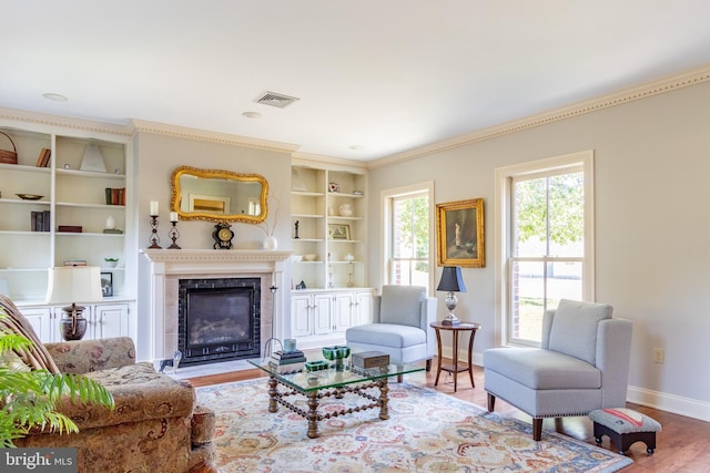 living room featuring a tile fireplace, built in features, visible vents, baseboards, and wood finished floors