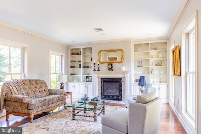 living area featuring wood finished floors, built in features, visible vents, a fireplace with flush hearth, and crown molding