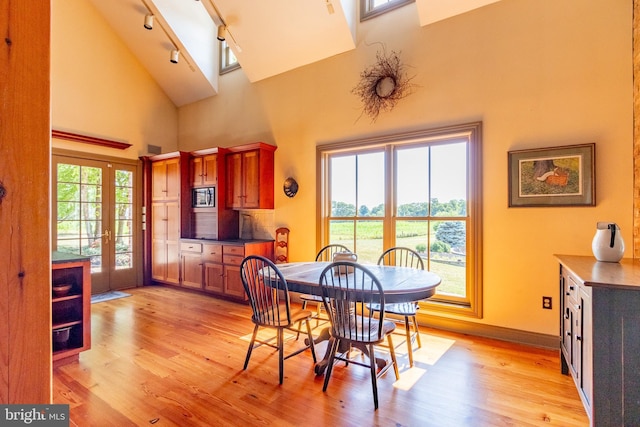 dining area featuring track lighting, light wood finished floors, high vaulted ceiling, and baseboards