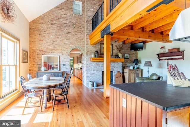 interior space with arched walkways, brick wall, a fireplace, wood finished floors, and high vaulted ceiling