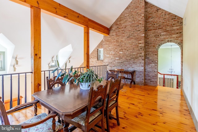 dining space featuring a chandelier, brick wall, hardwood / wood-style floors, and high vaulted ceiling