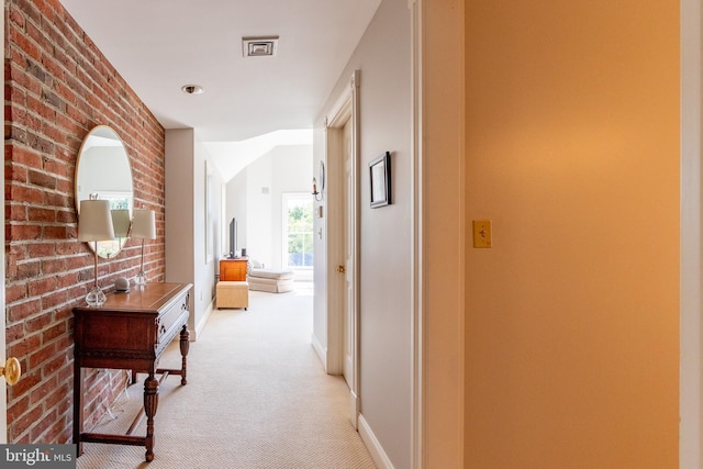 corridor featuring light colored carpet, visible vents, brick wall, and baseboards