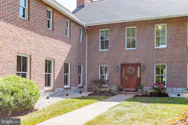 view of front of home featuring a chimney, brick siding, a front lawn, and roof with shingles