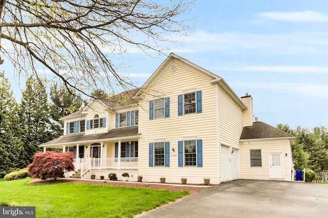 traditional-style home with a chimney, a porch, a garage, driveway, and a front lawn
