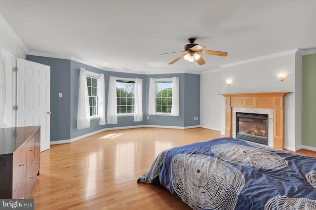 bedroom with crown molding, light wood-style floors, a high end fireplace, baseboards, and a ceiling fan