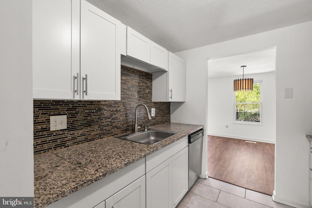kitchen featuring stainless steel dishwasher, a sink, decorative backsplash, light tile patterned floors, and white cabinetry