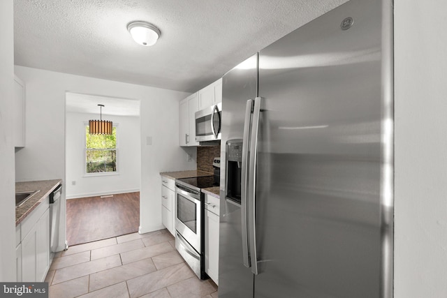 kitchen with light stone counters, tasteful backsplash, a textured ceiling, white cabinetry, and appliances with stainless steel finishes