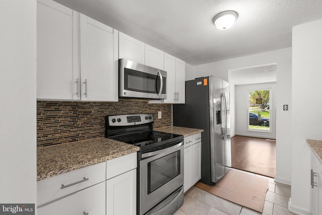 kitchen featuring white cabinets, stainless steel appliances, backsplash, stone countertops, and light tile patterned flooring