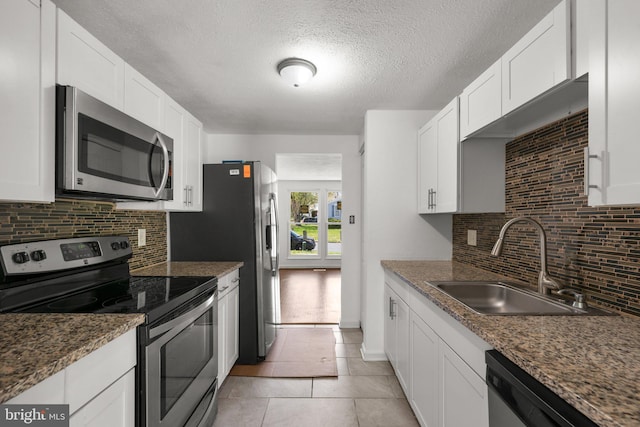 kitchen featuring a textured ceiling, a sink, backsplash, white cabinetry, and appliances with stainless steel finishes