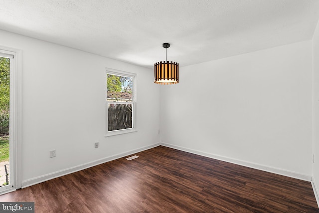 empty room featuring baseboards, dark wood-style flooring, and visible vents