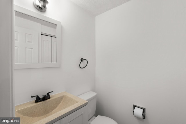 half bathroom with vanity, a textured ceiling, and toilet