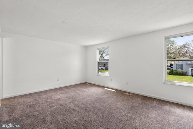 carpeted spare room with plenty of natural light, visible vents, and baseboards