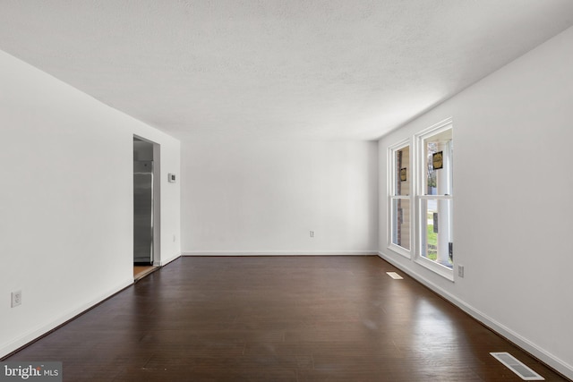 spare room featuring dark wood finished floors, baseboards, a textured ceiling, and visible vents