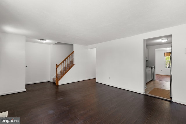 unfurnished living room featuring stairway, baseboards, and wood finished floors
