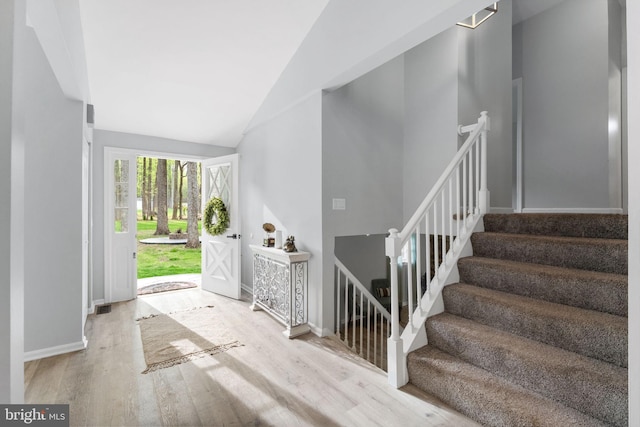 foyer entrance with lofted ceiling, baseboards, wood finished floors, and stairs