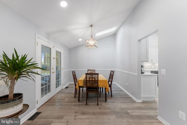 dining space featuring french doors, light wood-type flooring, visible vents, a chandelier, and vaulted ceiling with skylight