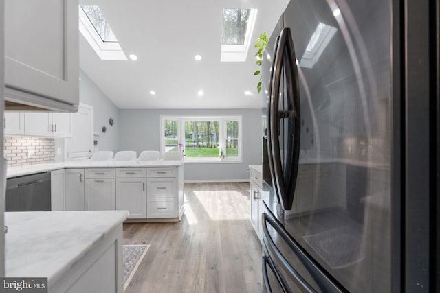 kitchen featuring dishwasher, light wood-style flooring, a skylight, and freestanding refrigerator
