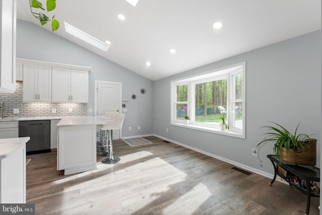 kitchen with lofted ceiling with skylight, a breakfast bar area, dishwasher, backsplash, and visible vents