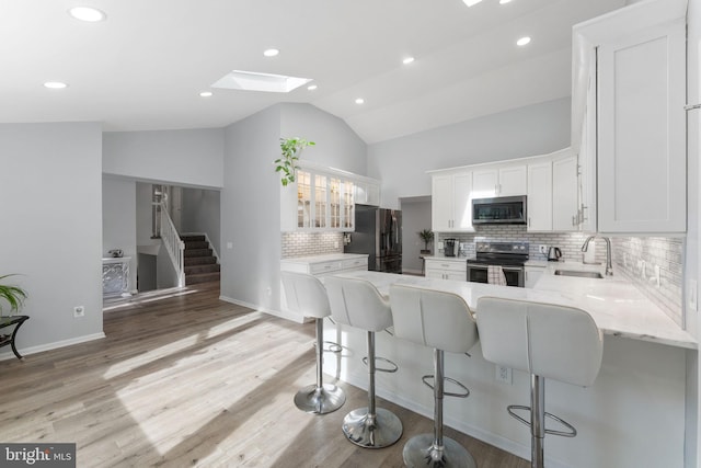 kitchen with stainless steel appliances, a sink, decorative backsplash, vaulted ceiling with skylight, and white cabinetry