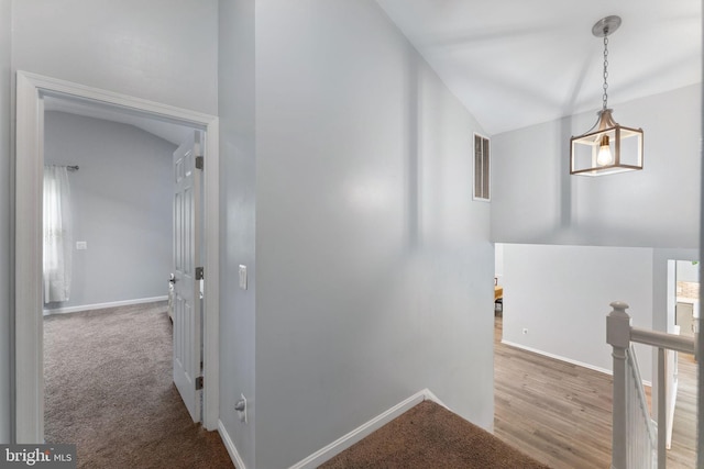 hall with vaulted ceiling, visible vents, baseboards, and an upstairs landing