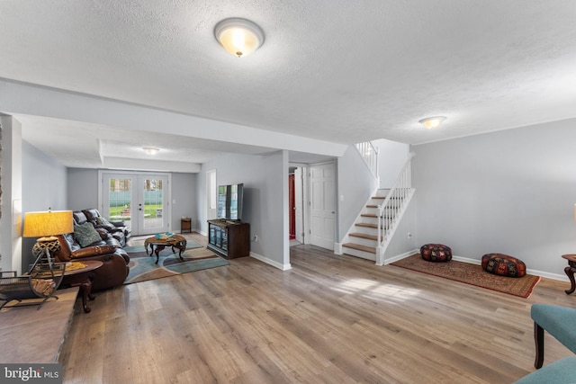 living room with baseboards, a textured ceiling, light wood finished floors, and stairs