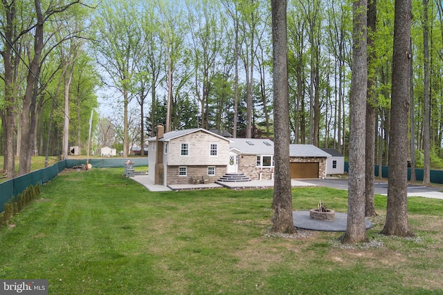 exterior space with a front lawn, a fire pit, stone siding, a chimney, and concrete driveway