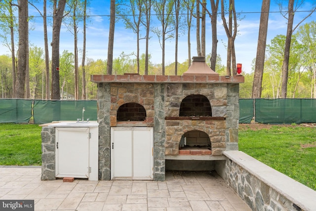 view of patio with fence, an outdoor stone fireplace, and a sink