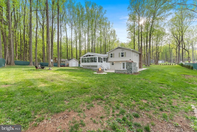 back of property with a chimney, an outdoor structure, a lawn, a fire pit, and a sunroom