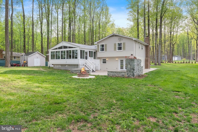 rear view of property featuring a chimney, an outdoor structure, an outdoor fire pit, a storage unit, and a sunroom