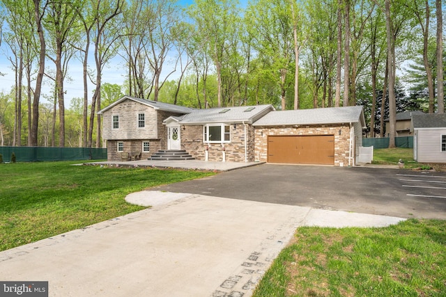 tri-level home with a front lawn, aphalt driveway, stone siding, fence, and a garage