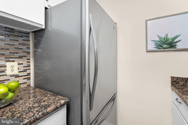 kitchen with white cabinets, decorative backsplash, freestanding refrigerator, and dark stone countertops