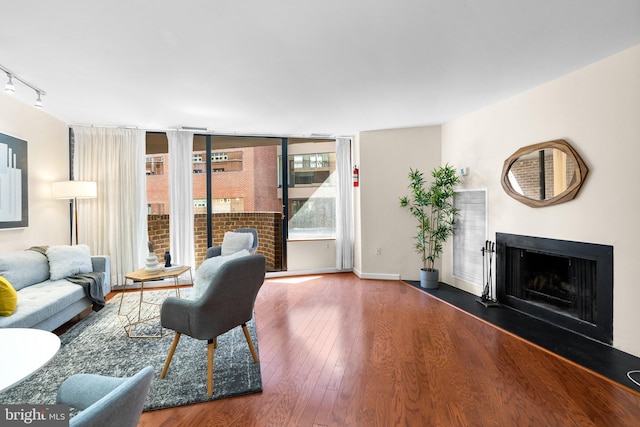 living room featuring a fireplace with flush hearth, wood-type flooring, rail lighting, and baseboards