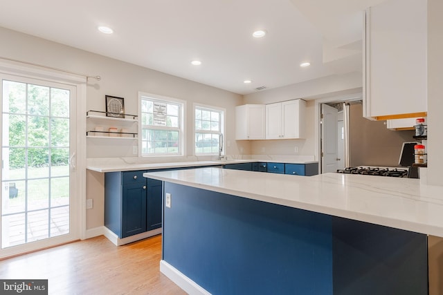 kitchen featuring blue cabinets, a peninsula, light wood finished floors, recessed lighting, and light stone counters