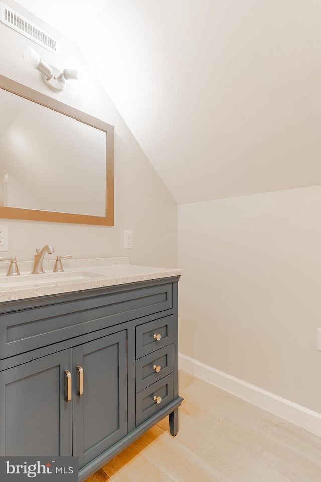 bathroom with lofted ceiling, vanity, baseboards, and wood finished floors