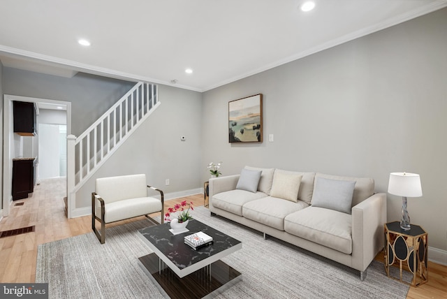 living area with crown molding, light wood finished floors, baseboards, and stairway